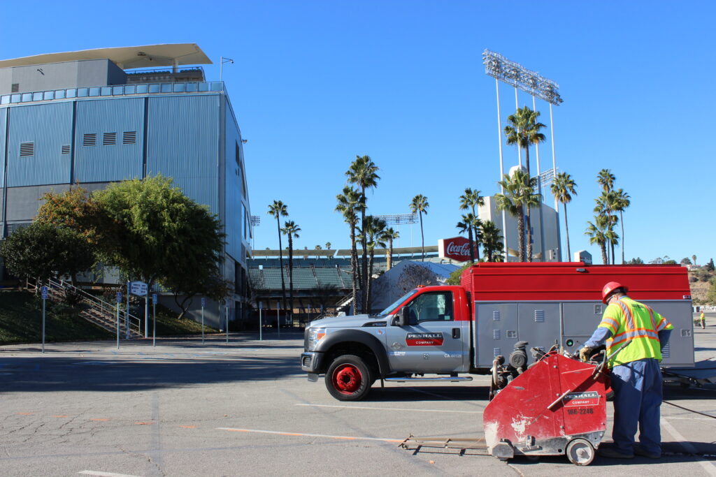penhall empployee using concrete cutter with penhall truck and palm trees in background